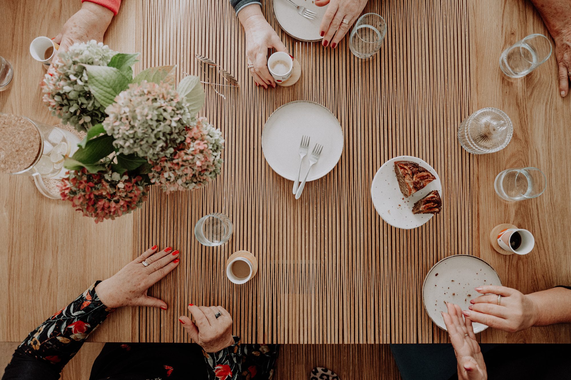 Friends' hands around the open table, with flowers, cake and coffee