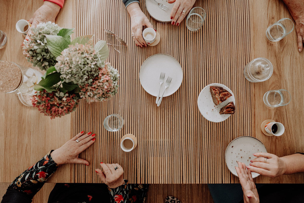 Plates, glasses and hydrangeas on the open table, seen from above, with hands reaching in