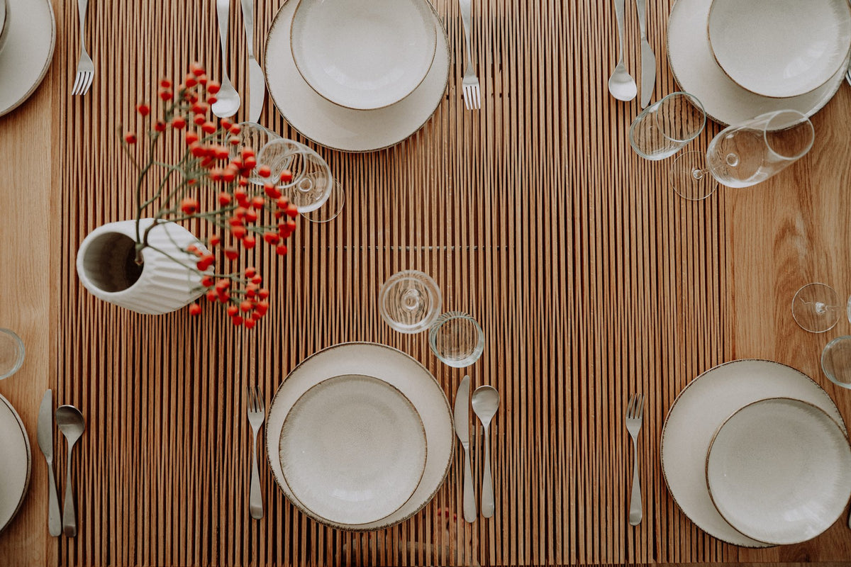 A holiday table from above: white plates, glasses and a vase of red berries on the oak