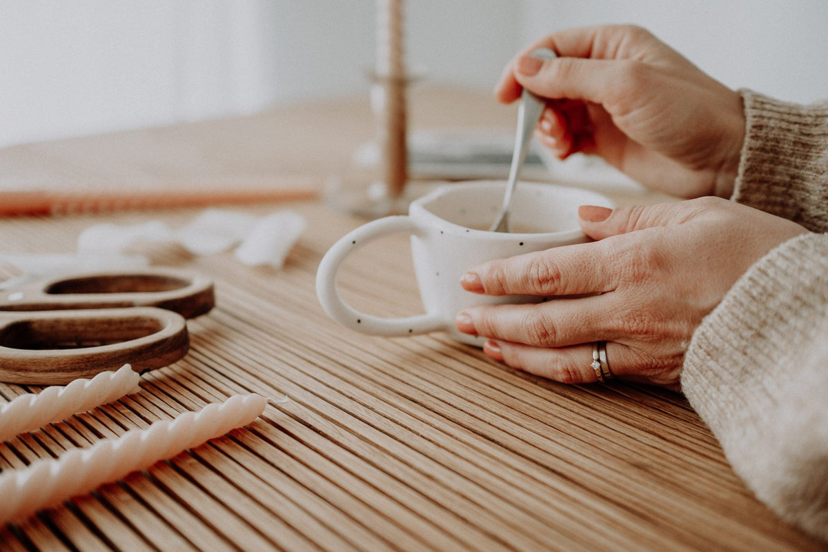 Hands around a speckled coffee cup on the oak table, twisted candles beside it