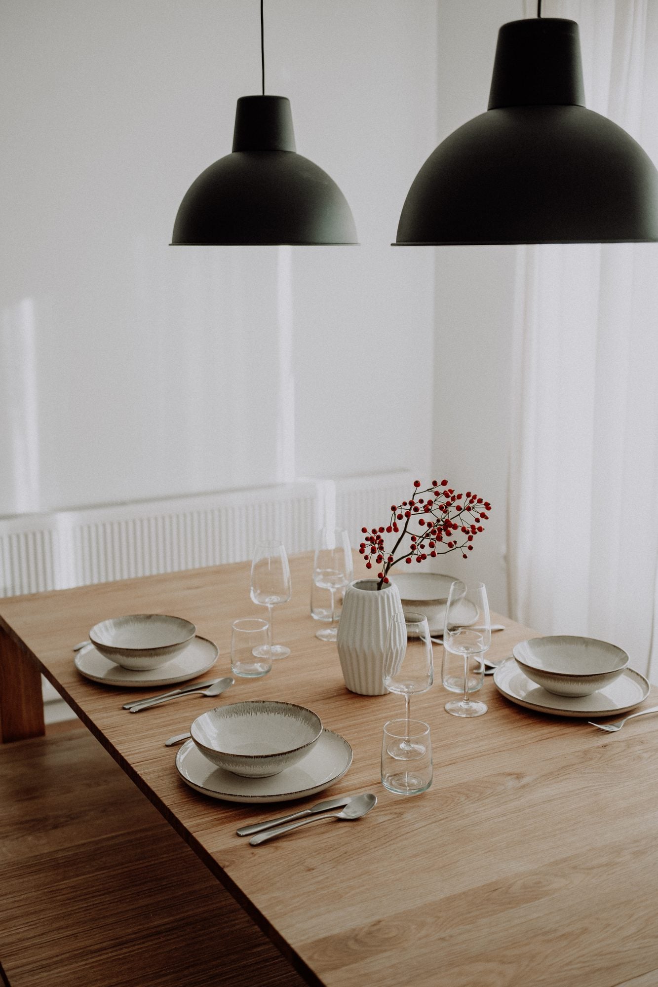 The oak table set for guests, with red berries in a vase