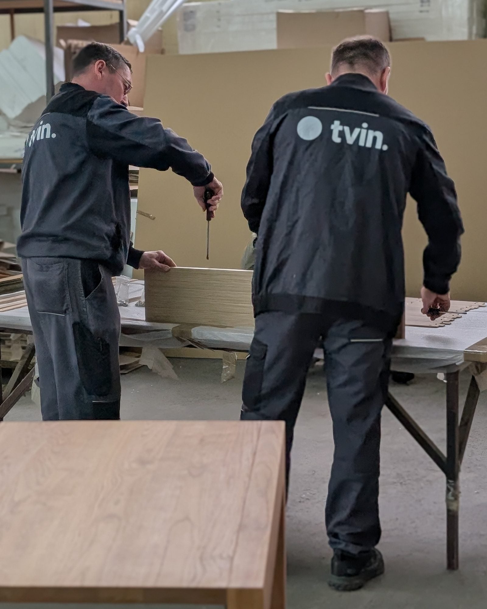 Two Tvin makers fitting the lattice with screwdrivers, a finished table in front